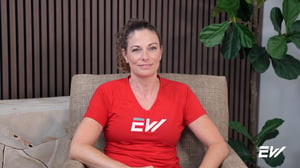 Woman in red t-shirt sits in comfortable brown chair to discuss her positive experience with a personal trainer