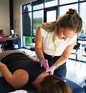 Female physical therapist performing dry needling on a patient's upper back and shoulder trigger points for muscle pain relief and myofascial release at a physical therapy clinic.