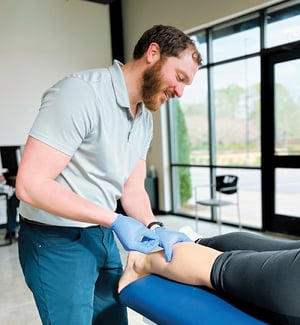 Physical therapist performing dry needling on patient's lower leg and ankle for pain relief and trigger point therapy.