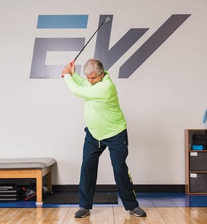 Older adult golfer demonstrating a full backswing during a golf-specific physical therapy assessment for back, shoulder, and hip injury rehabilitation at a PT clinic.