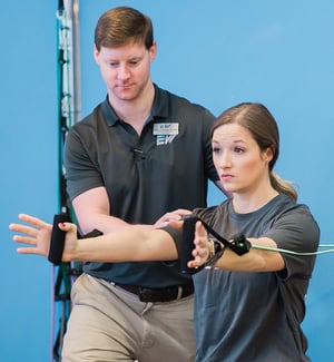 Physical therapist guiding patient through resistance band rotator cuff exercise for orthopedic shoulder rehabilitation.