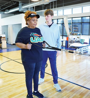 Physical therapist supervising senior patient performing resistance band exercise for orthopedic upper body rehabilitation.