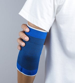 Person wearing an elbow compression sleeve for support and pain relief, commonly used in physical therapy and injury recovery.