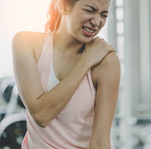 Woman holding her shoulder in pain during exercise, illustrating shoulder injury commonly treated with physical therapy.