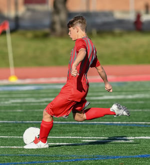 Youth soccer player kicking a ball on a field, illustrating athletic movement and lower-extremity demands addressed in sports physical therapy.