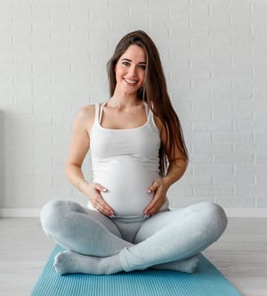 Pregnant woman sitting on a yoga mat practicing prenatal exercise, supporting pregnancy wellness and physical therapy care.