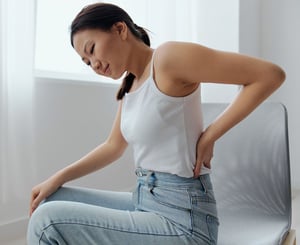 Woman sitting and holding her lower back, indicating back pain.