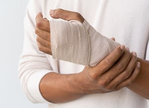 Person wearing a compression bandage on the wrist and hand to support a wrist injury.