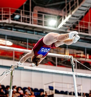 Competitive gymnast performing a strength move on the parallel bars during a gymnastics competition.