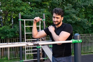 Man experiencing shoulder pain during outdoor exercise, holding his shoulder due to a sports-related injury commonly treated with physical therapy.
