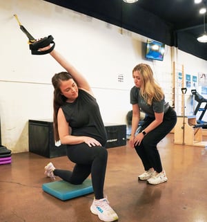 Women’s health physical therapist coaching a patient through a functional strength exercise using suspension straps, focusing on core stability, pelvic control, hip strength, and safe movement as part of women’s health physical therapy.