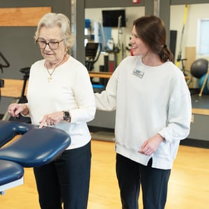Compassionate physical therapist performing balance therapy on elderly patient in bright spacious physical therapy and rehabilitation gym.