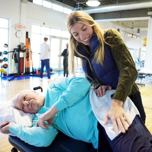 Compassionate physical therapist performing manual spinal therapy on elderly patient in bright spacious physical therapy and rehabilitation gym.