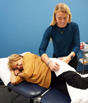 Physical therapist providing hands-on manual therapy to a patient’s hip while side-lying on a treatment table.