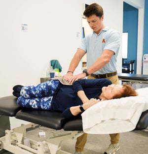 Physical therapist providing hands-on manual therapy to an older adult patient during a treatment session.