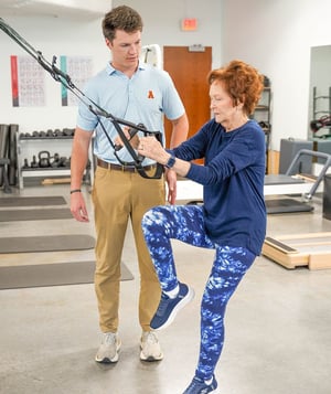 Physical therapist guiding an older adult through balance and strength training exercises in a physical therapy clinic.