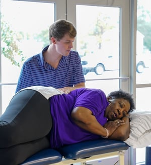 Physical therapist performing hands-on manual therapy to a patient’s lower back while side-lying.