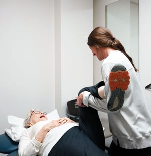 Physical therapist assisting an elderly woman with a knee stretch during a rehabilitation session.