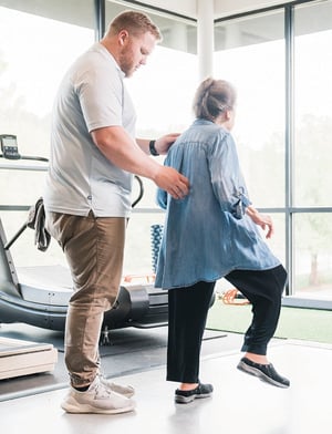 Physical therapist assisting an older adult with balance training exercise in a clinic.