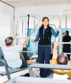 Physical therapist instructing group Pilates reformer class with male clients at EW Motion Therapy.