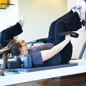 Client performing supine legs-in-straps reformer Pilates exercise for core and hip strengthening in Homewood Alabama.