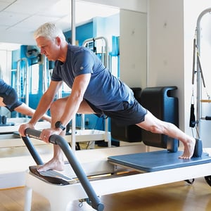 Older adult male client performing standing lunge and core stability exercise on Pilates reformer in Homewood Alabama clinical Pilates studio.