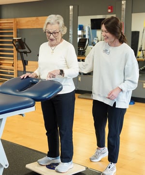 Physical therapist guiding elderly patient through balance board training exercise at EW Motion Therapy.
