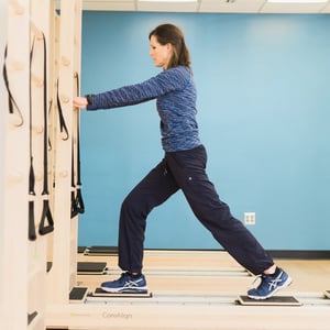 CoreAlign Pilates rehabilitation exercise showing a patient in a forward lunge position on sliding footplates for hip stability and postural alignment training.