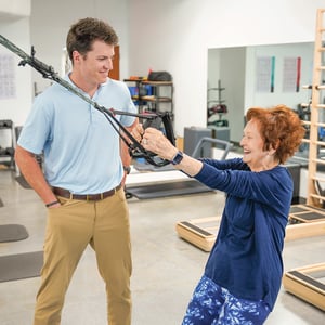 Physical therapist supervising orthopedic resistance band exercise in a physical therapy clinic.