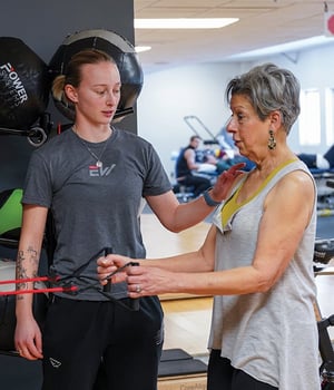 Personal trainer coaching older adult client on resistance band handle technique at EW Motion Therapy.