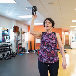 Senior woman performing kettlebell overhead press for functional strength and active aging fitness at EW Motion Therapy.
