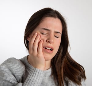 Woman experiencing jaw pain related to teeth grinding.