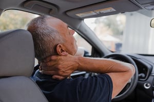 Man experiencing neck pain and whiplash while sitting in a car.