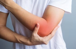 Person holding their elbow with visible redness, representing elbow pain or overuse injury that may benefit from physical therapy.